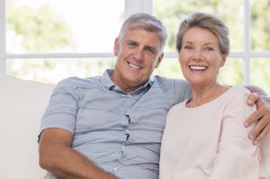 Smiling senior woman, and man sitting together on a sofa. Portrait of a candid older couple enjoying their retirement at home. Happy smiling senior couple embracing together and looking at camera.